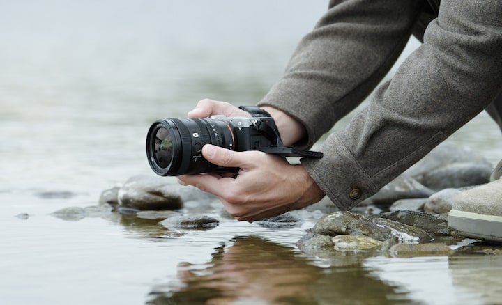 강 표면 가까이에서 FE 24-50mm F2.8 G를 장착한 α7CII를 들고 있는 사용자를 보여주는 사용 이미지. 사용자는 낮은 자세로 촬영하고 있음